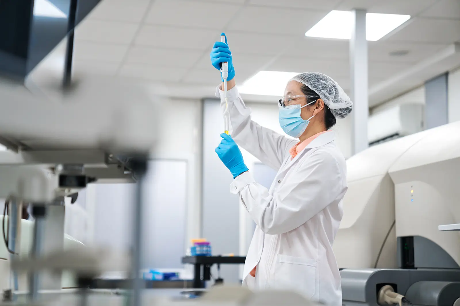 A scientist in a lab coat and face mask using a pipette in a modern research laboratory.